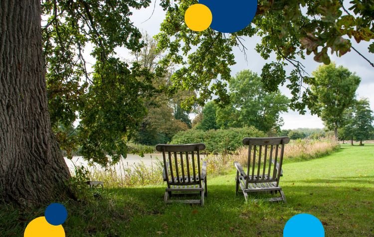 two chairs by the side of a lake on the grass